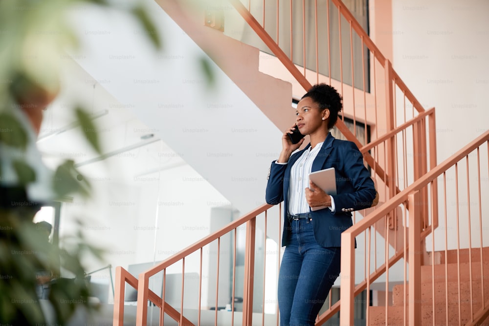 Black businesswoman communicating over cell phone while walking down the stairs in the office.