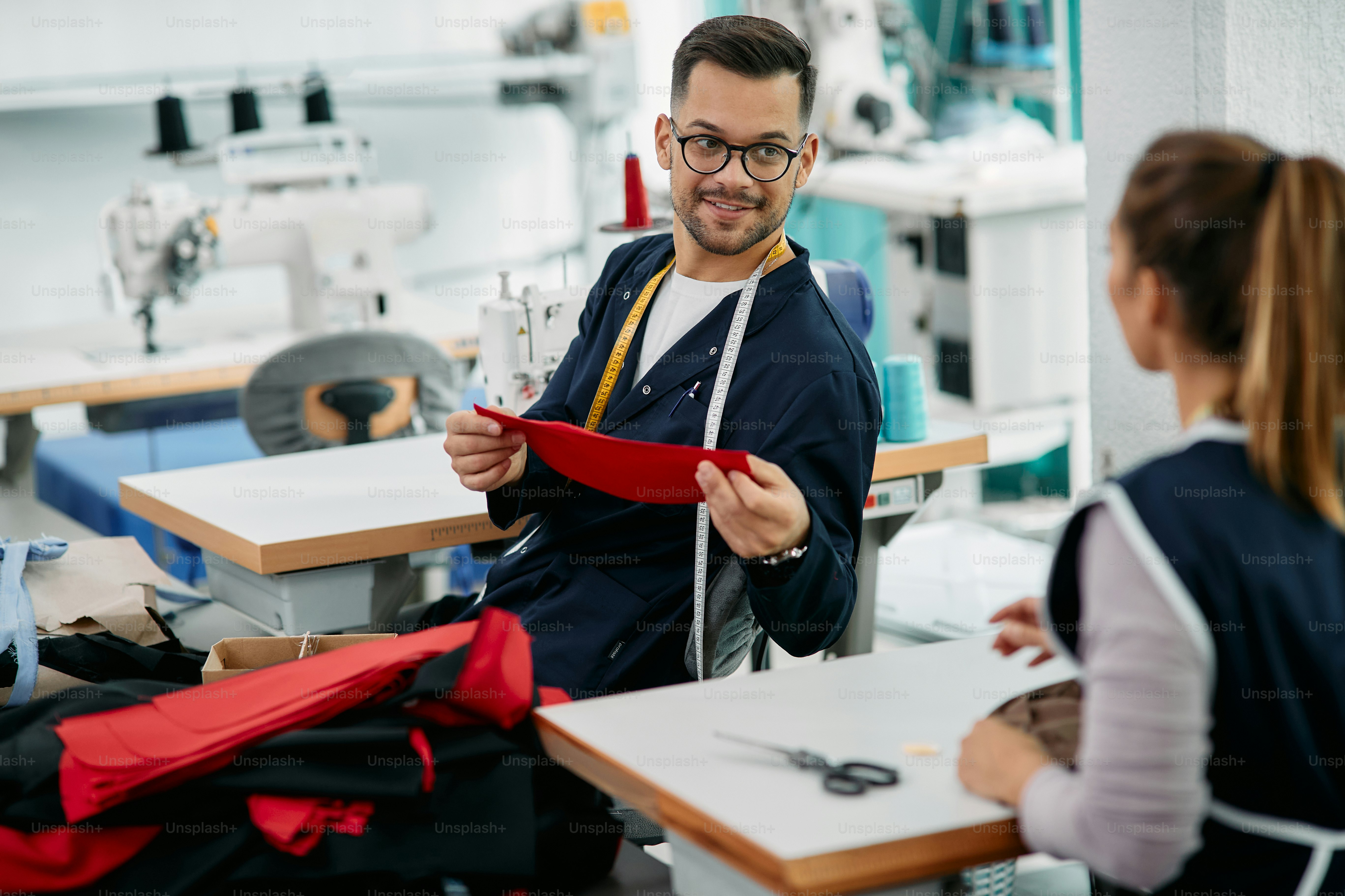 Young tailor communicating with female coworker while sewing at ...