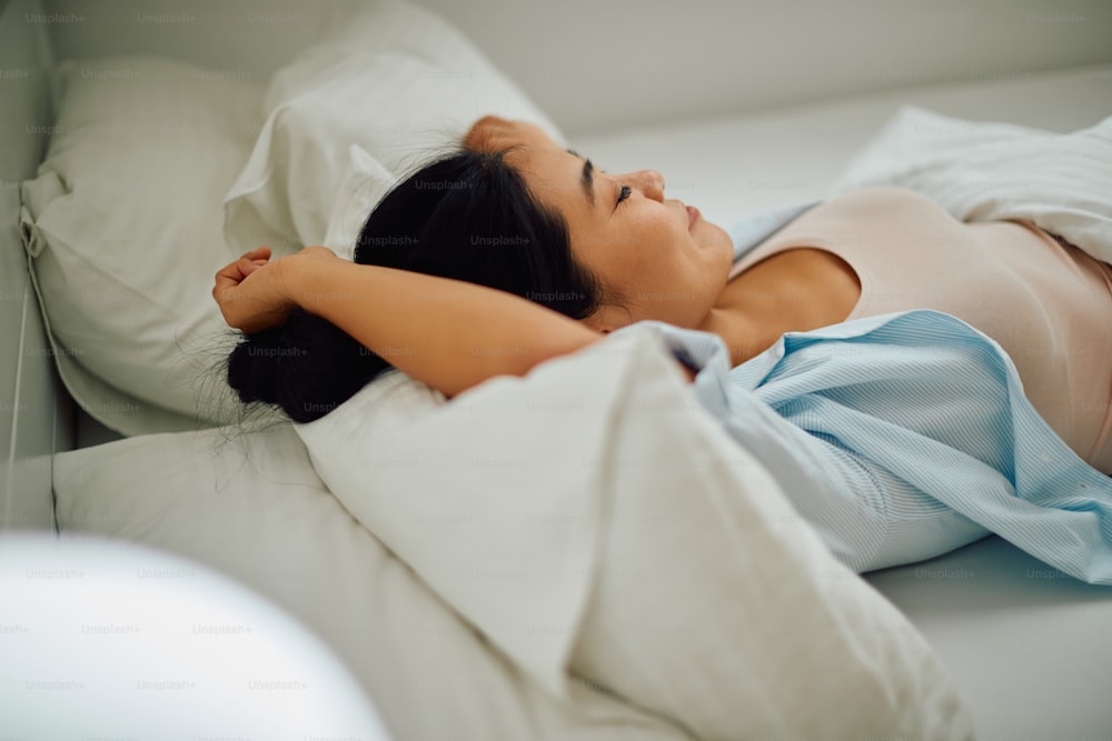 Giovane donna asiatica che riposa mentre è sdraiata sulla schiena in un letto.