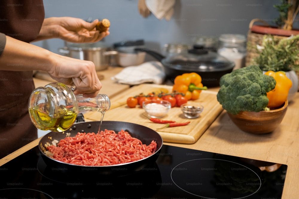 집에서 전통적인 이탈리아 파스타를 요리하는 동안 생 다진 고기로 프라이팬에 올리브 오일을 붓는 여자의 손