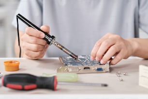 Mani di giovane tecnico contemporaneo con saldatore che ripara la scheda madre con microchip