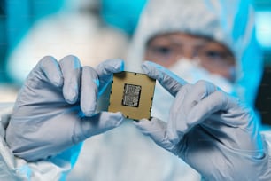 Manos enguantadas de un científico contemporáneo o de un ingeniero informático con ropa de trabajo protectora que sostiene un microchip