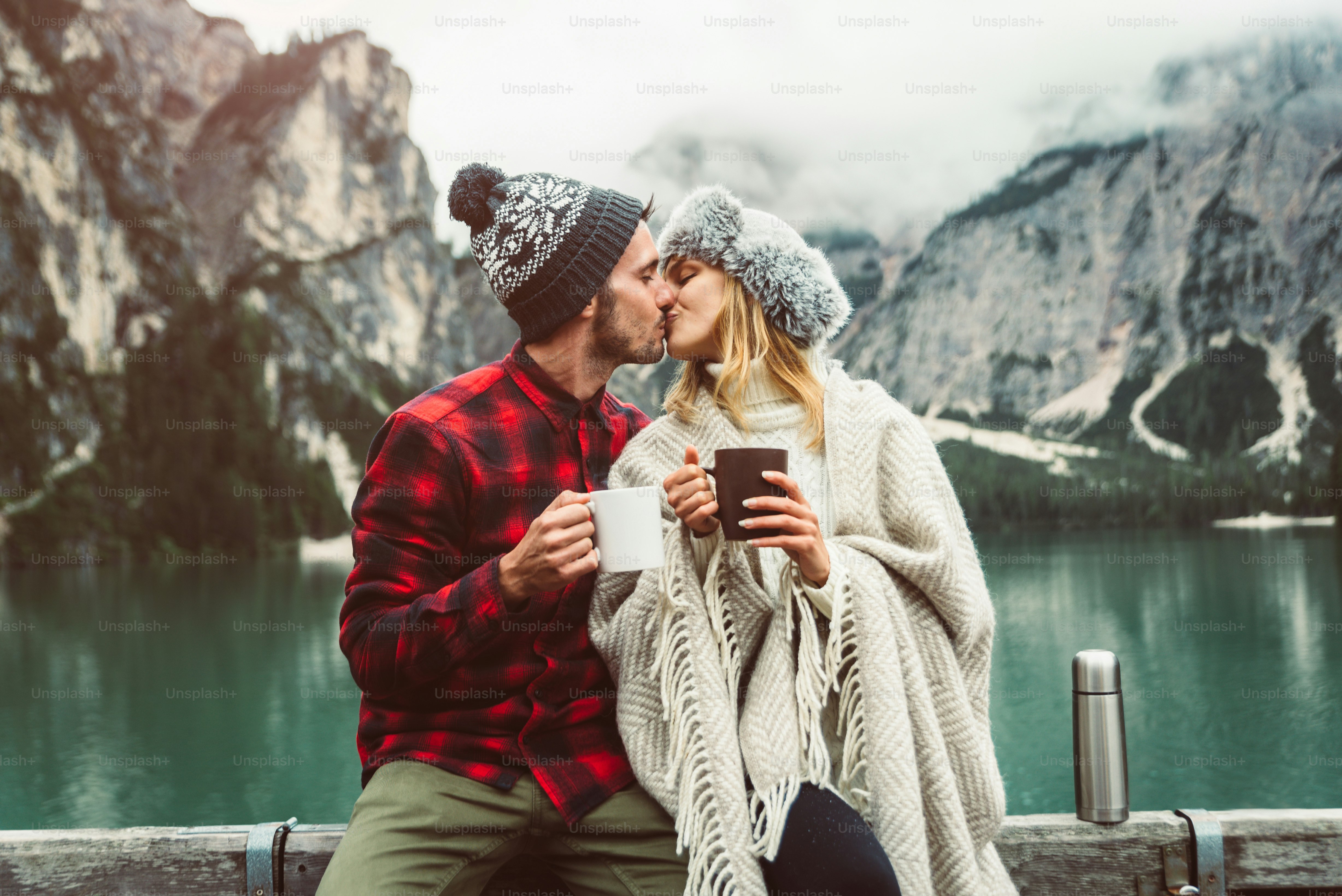 Portrait of a romantic couple of adults visiting an alpine lake at Braies Italy at winter. Tourist in love drinking hot coffee at mountains. Couple, wanderlust and travel concept.