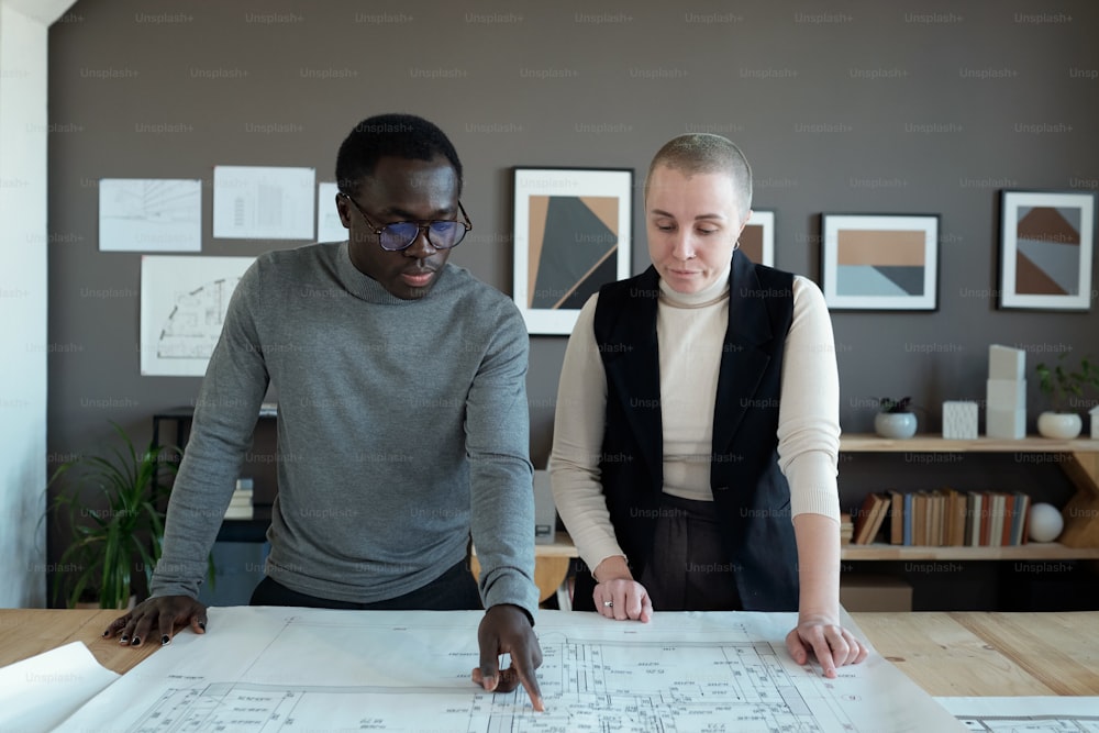 Arquitectos creativos contemporáneos discutiendo boceto sobre plano mientras uno de ellos señala notas de tamaño