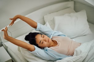 Giovane donna asiatica sorridente che si sveglia al mattino e si allunga su un letto.