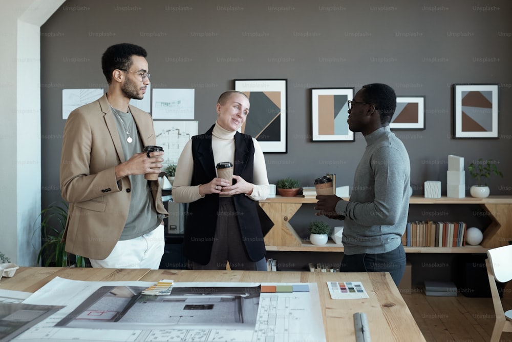 Equipo de diseñadores creativos tomando unas copas mientras discuten ideas de diseño de interiores para un nuevo apartamento en una reunión de trabajo