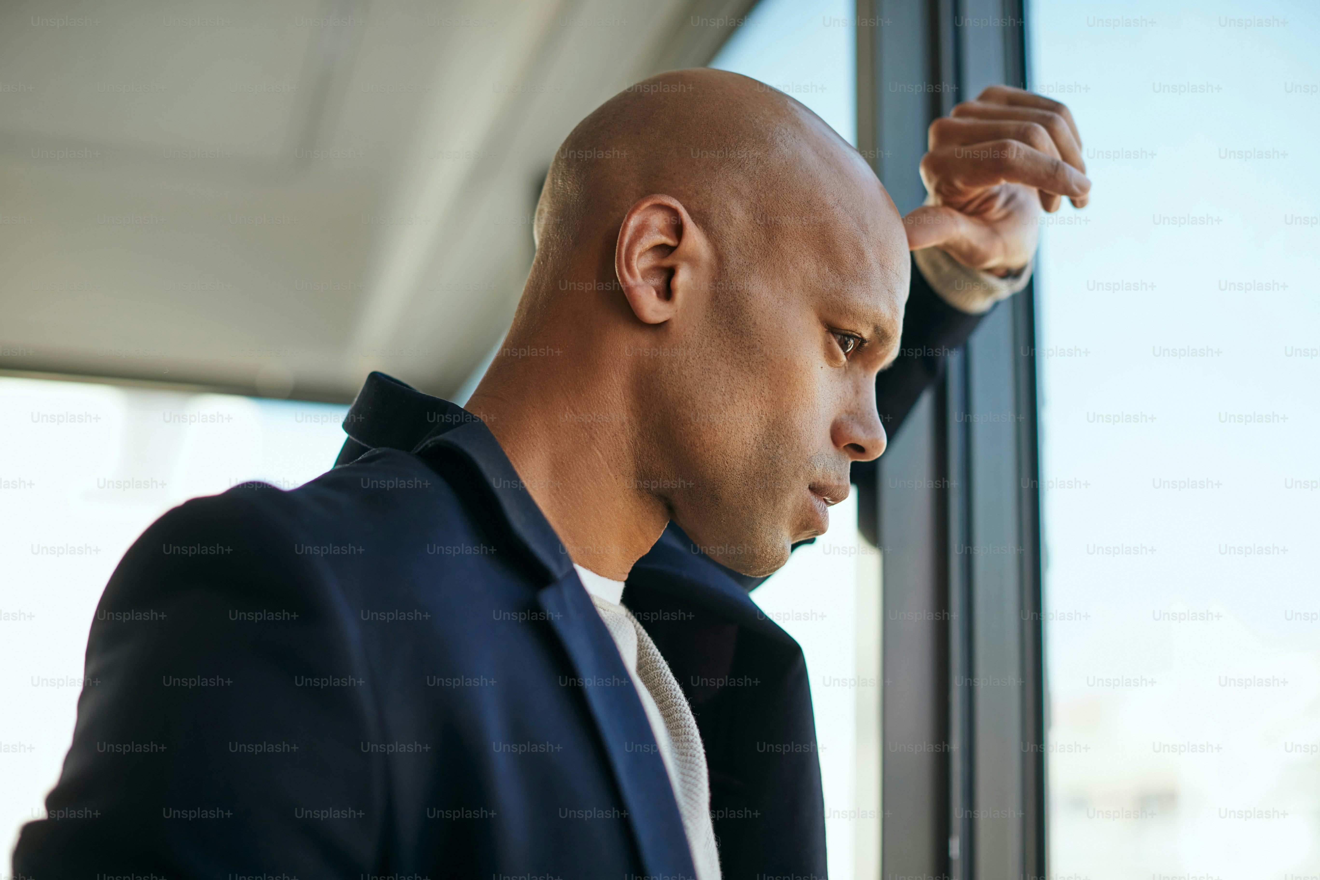 African American businessman thinking of something while looking through the widow of his office.