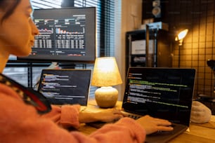Mujer escribiendo código de programación en computadoras portátiles y computadoras de escritorio en un lugar de trabajo acogedor en casa. Concepto de trabajo de programador remoto en casa