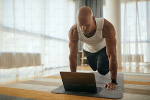 African American athlete following online exercise class over laptop while working out at home. Copy space.