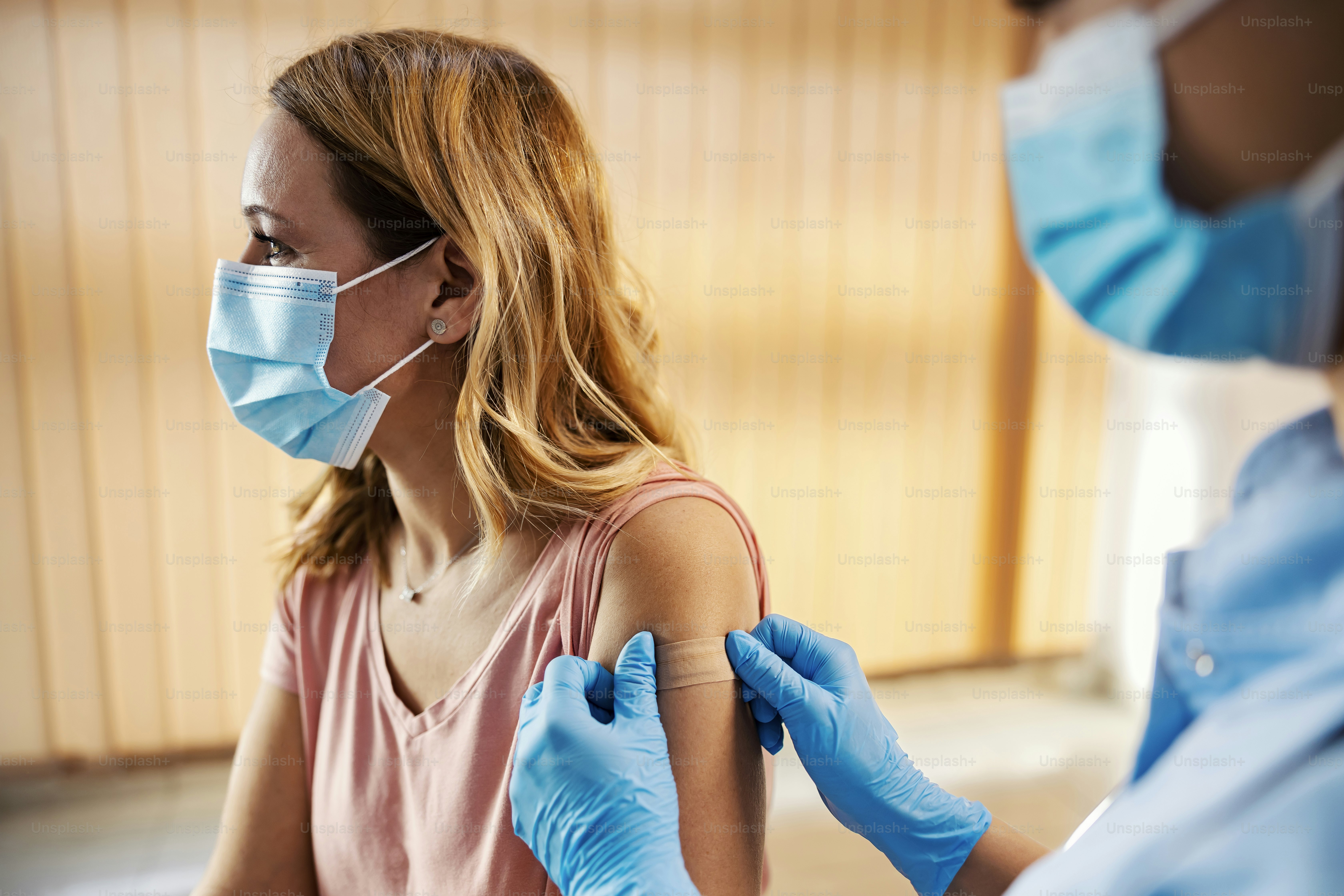 A nurse in hospital putting adhesive plaster on woman's arm after covid 19 vaccine. Immunization, vaccination and medical care.