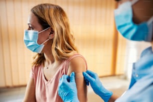 Una enfermera en el hospital colocando un yeso adhesivo en el brazo de una mujer después de la vacuna contra el covid 19. Inmunización, vacunación y atención médica.