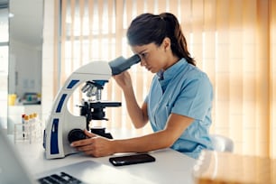 A lab assistant in lab using microscope for tests. Medical support, lab tests and medical service.