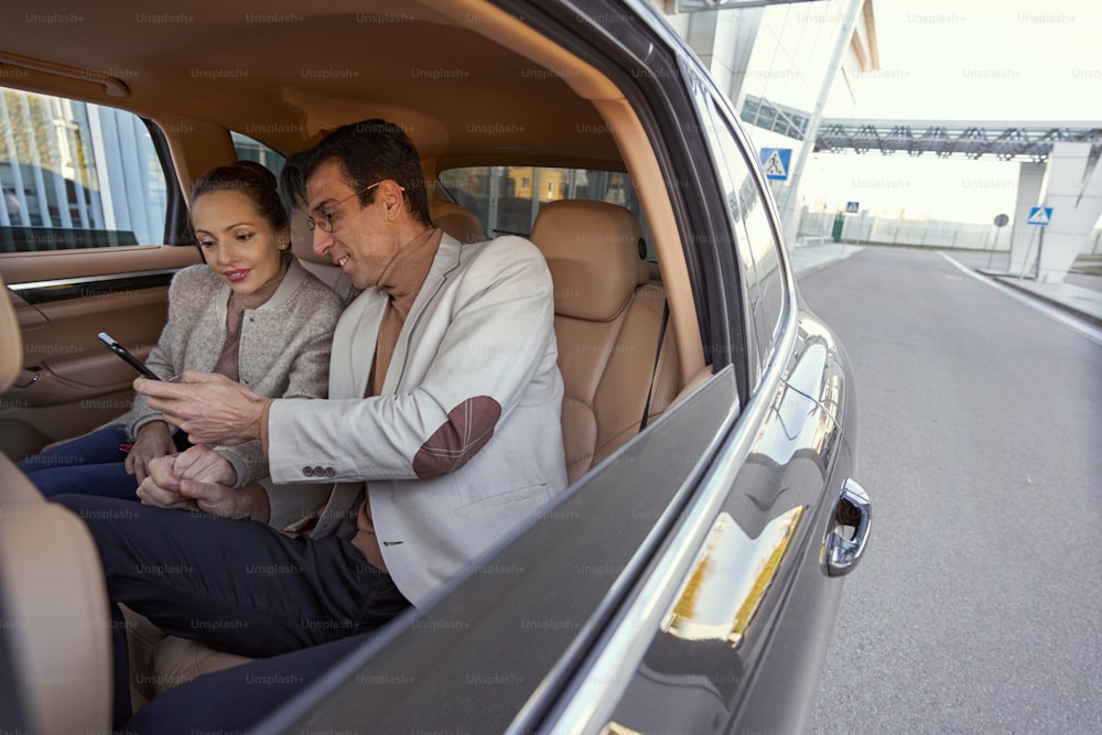 Frau hält Hand eines kaukasischen Mannes auf dem Rücksitz des Autos, während er das Telefonat beendet