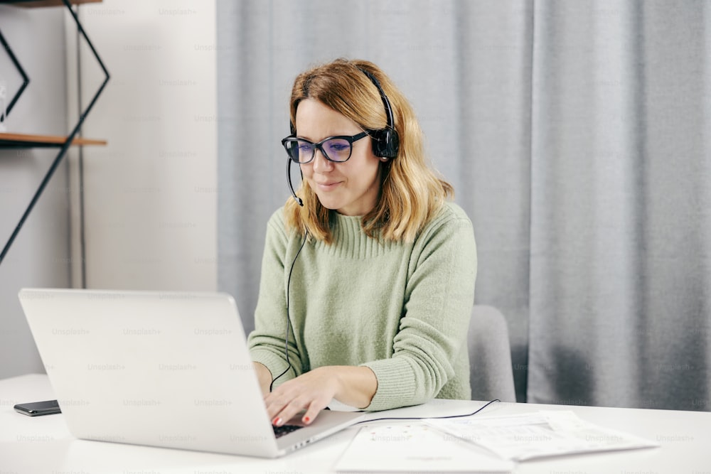 Una teletrabajadora feliz de mediana edad en la oficina en casa trabajando en línea en su computadora portátil.