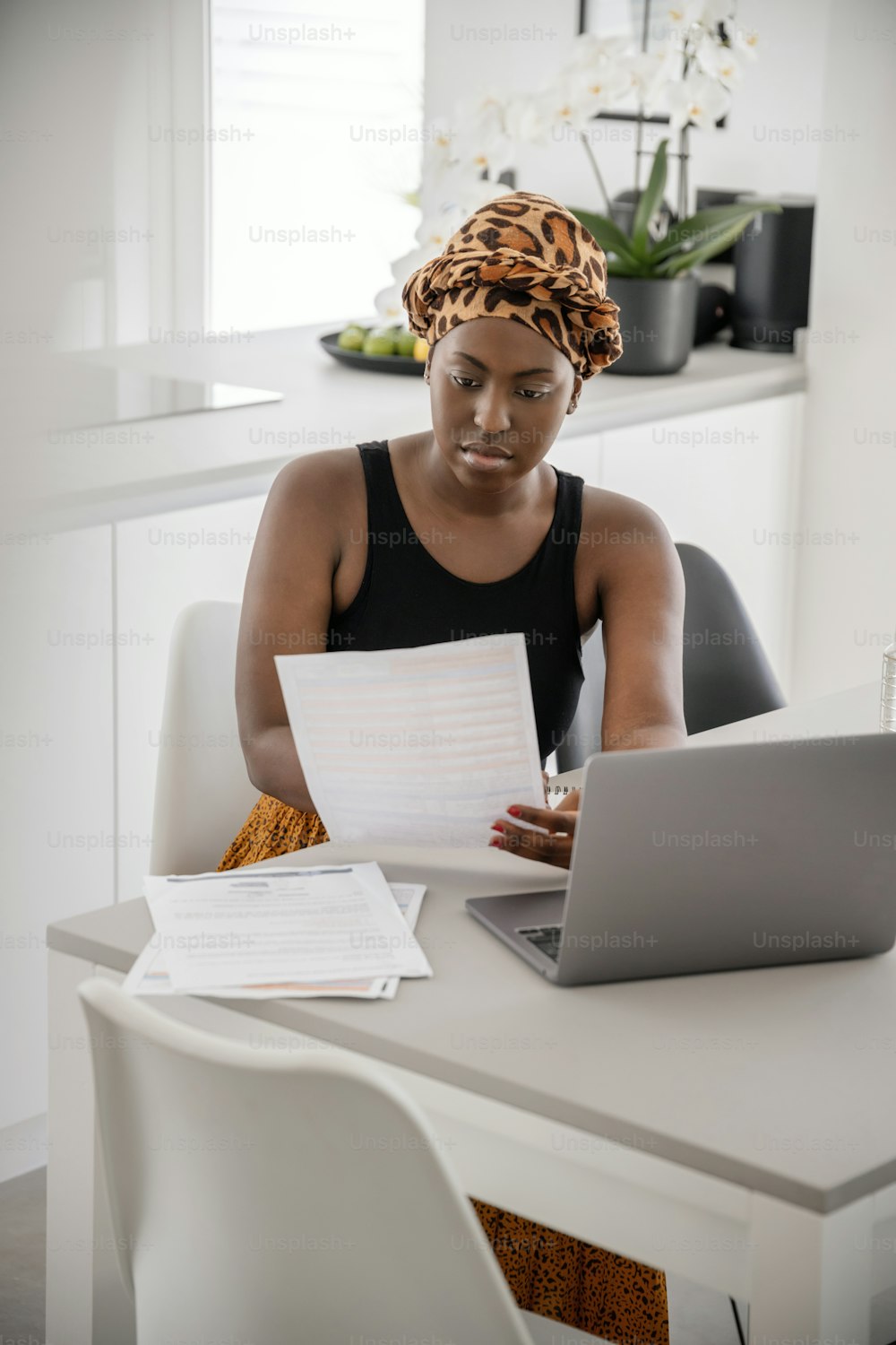 Black African woman working from home, going through paperwork. Laptop and smartphone on home office table