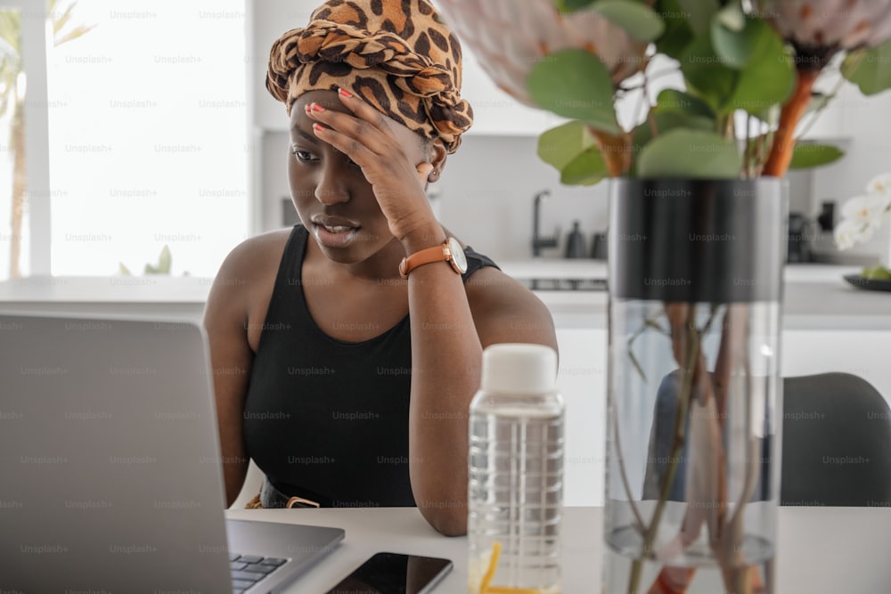 Young Black African woman tired, exhausted from working studying hard from home. Bored and frustrated looking at laptop. Head resting on hand. Stress concept.