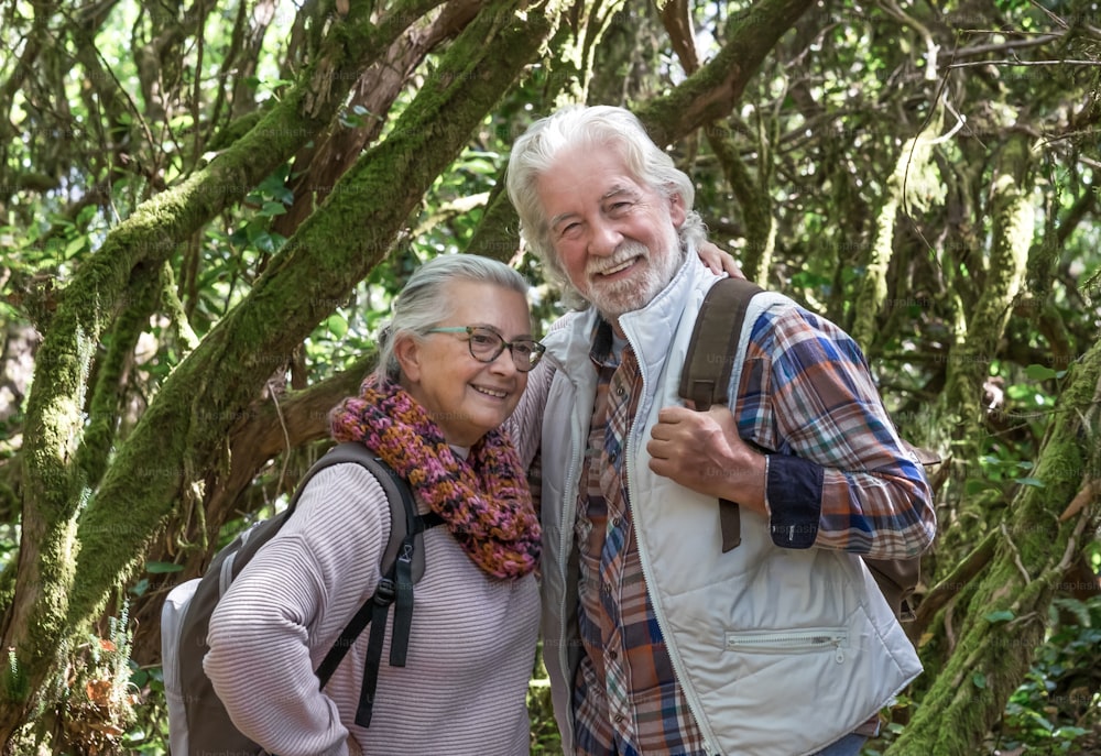 Loving mature adult happy senior couple enjoying mountain hike in the woods among trunks and branches covered with moss - active and healthy lifestyle concept during retirement