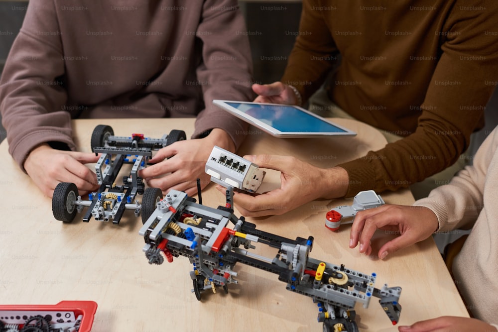 Nahaufnahme von Schülern, die Roboter mit digitalem Tablet am Tisch während des Ingenieurunterrichts verbinden