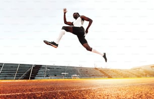 Esportista corre e pula treino em pista de corrida no estádio - Tiro completo de jovem africano saudável correndo ao ar livre - Conceito de estilo de vida esportivo