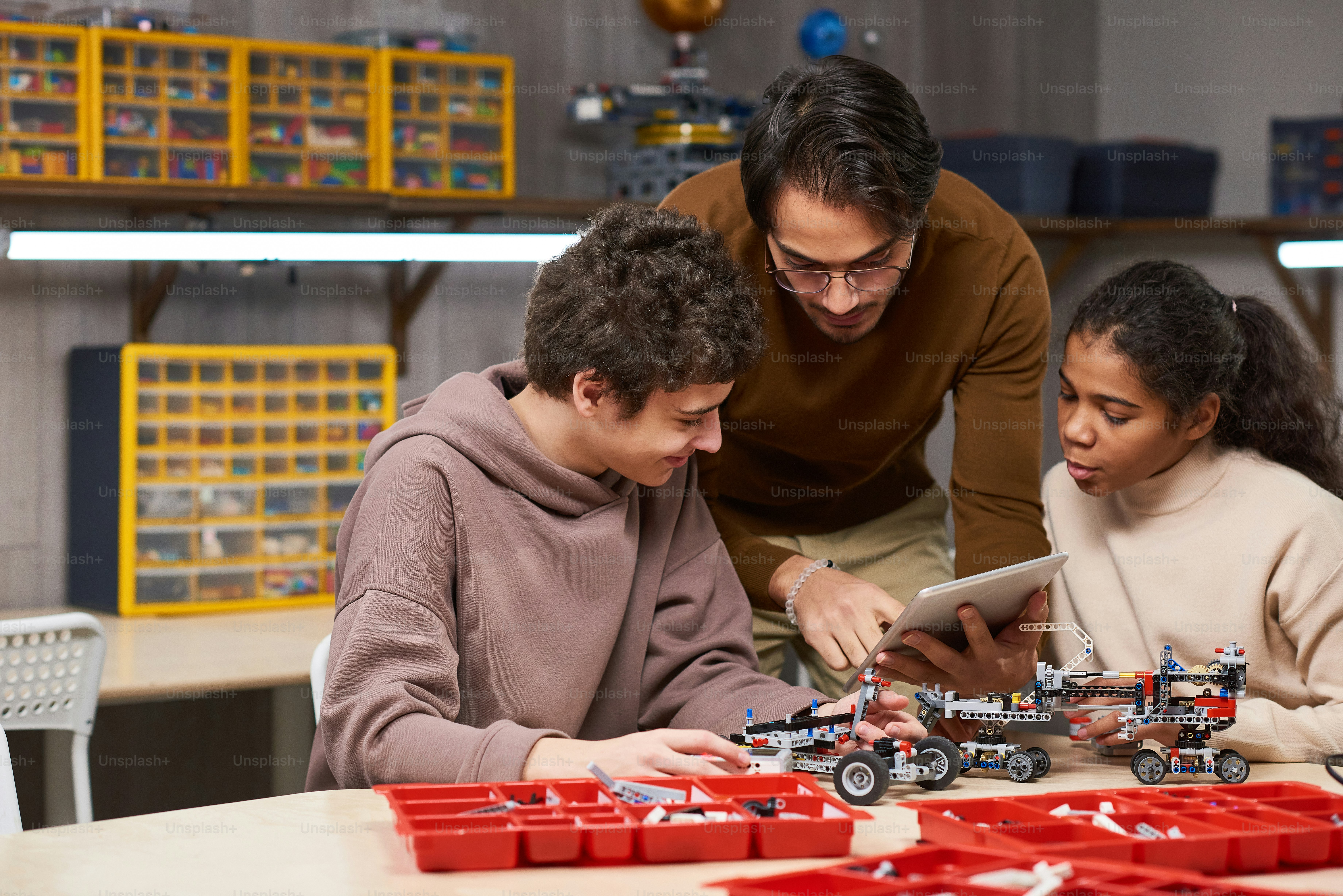 Young teacher helping children to connect robots with digital tablet while they sitting at the table