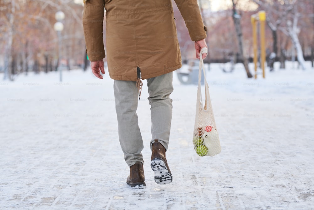 Rear view of old man walking the street home after shopping and carrying bag with grocery