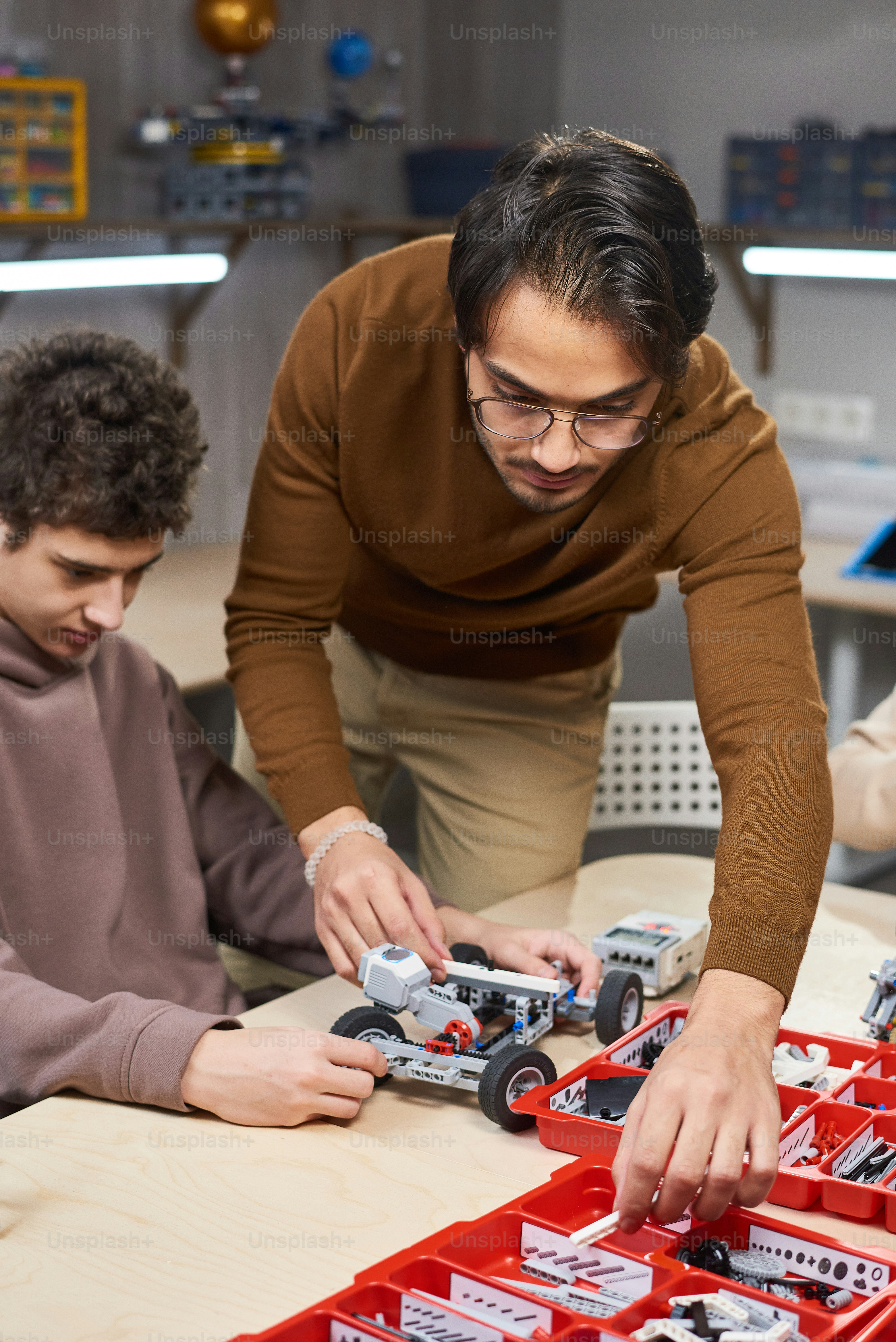 Teenager sitzt am Tisch und baut Roboter aus Konstruktordetails zusammen mit Lehrer im naturwissenschaftlichen Unterricht