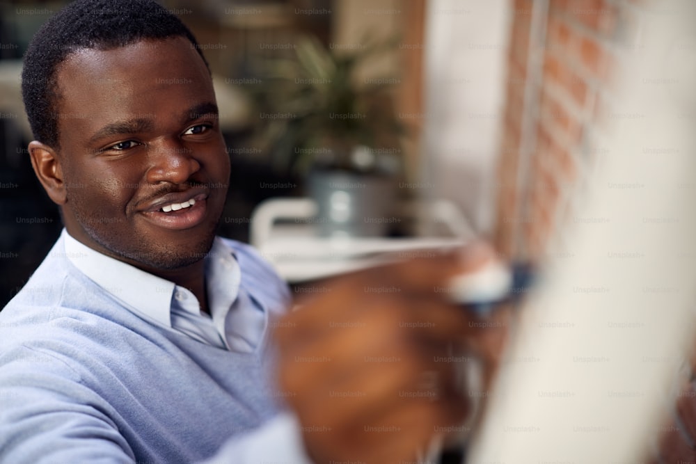 Feliz empreendedor afro-americano escrevendo no quadro branco enquanto realiza apresentação de negócios no escritório corporativo.