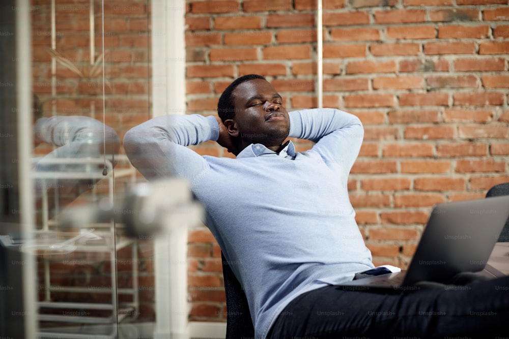 African American entrepreneur with hands behind head taking a break after working on a computer in the office.