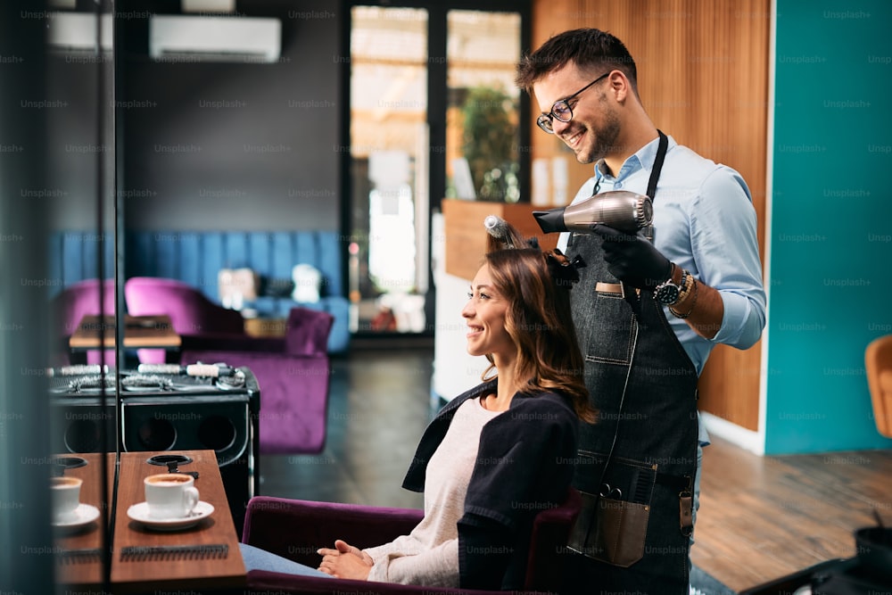 Coiffeur heureux coiffant les cheveux d’une jeune femme lors d’un rendez-vous au salon de coiffure.