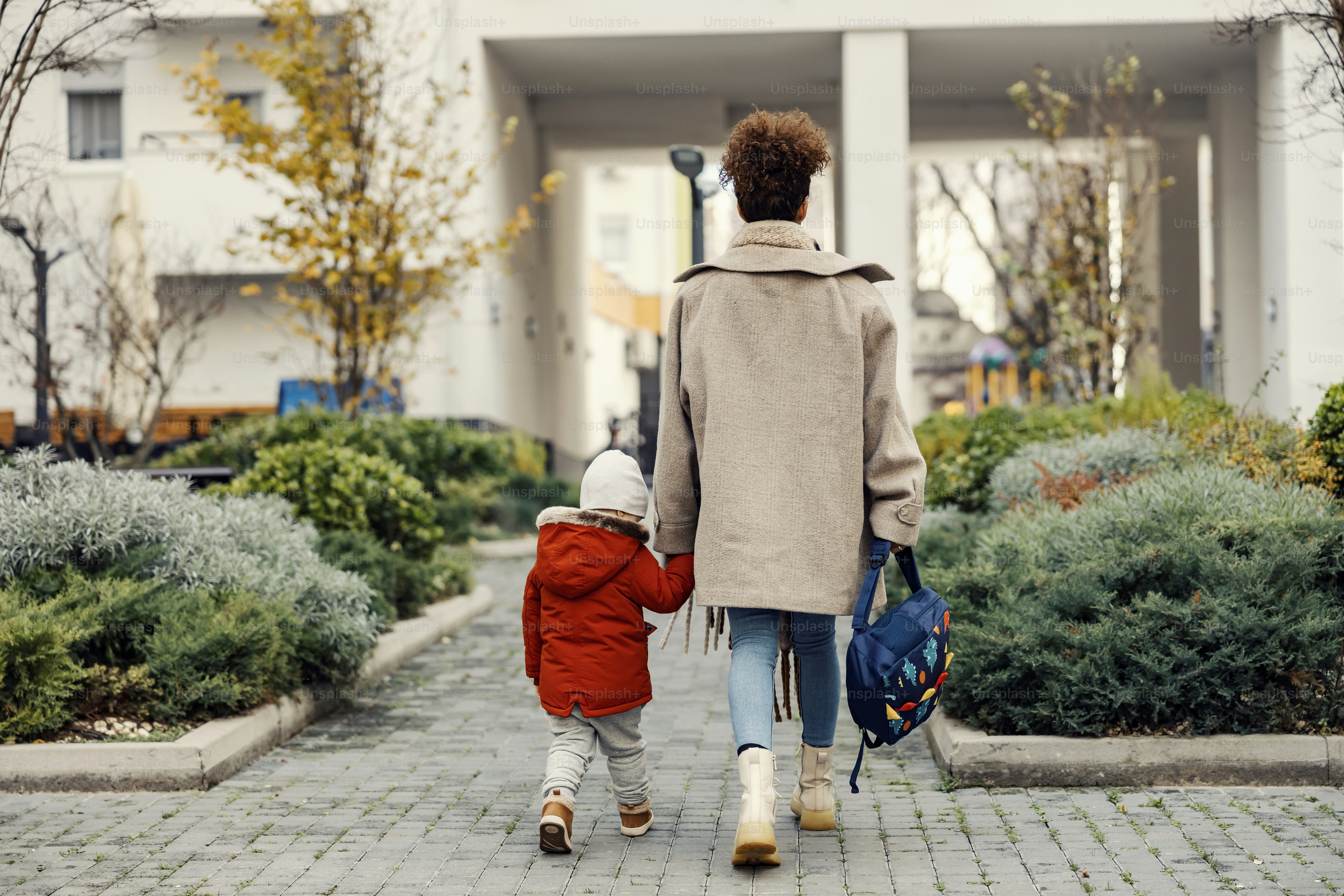 A mother holding hands with her little son and taking him home from kindergarten or daycare.