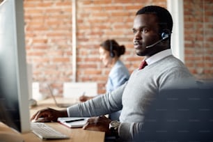 African American customer service representative wearing headset and using Desktop PC while working in the office.
