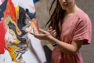 Gros plan d’un jeune artiste pointant du doigt une image peinte et en parlant lors d’une présentation dans un studio d’art
