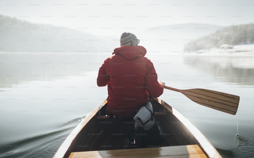 冬の晴れた日にカヌーを漕ぐ男性の背面図。
