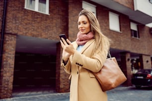 Rete Wi-Fi, comunicazioni globali e provider di telefonia mobile. Una giovane donna in abiti caldi in piedi sulla strada in un clima freddo e ventoso e digitando sul suo telefono cellulare.
