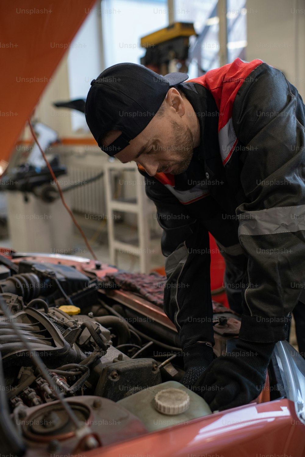 Vertical portrait of male mechanic looking under hood while repairing car in auto shop