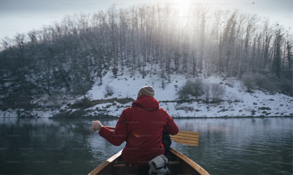 冬のカヌーに乗って漕ぐ男性の背面図。