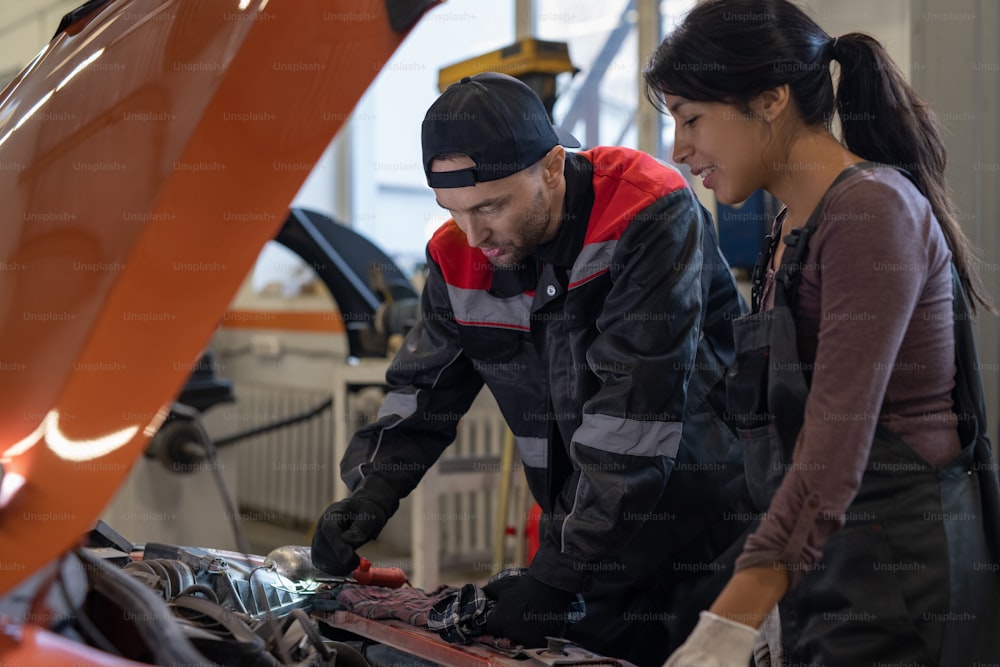 自動車修理工場で作業しながら車のエンジンを検査するボンネットの下を見ている2人の整備士の側面図の肖像画、コピースペース