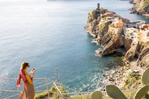 Woman enjoys beautiful landscape of coastline with old Vernazza village, traveling famous Cinque Terre towns in northwestern Italy. Summer vacation on the Mediterranean coast concept. Wide view