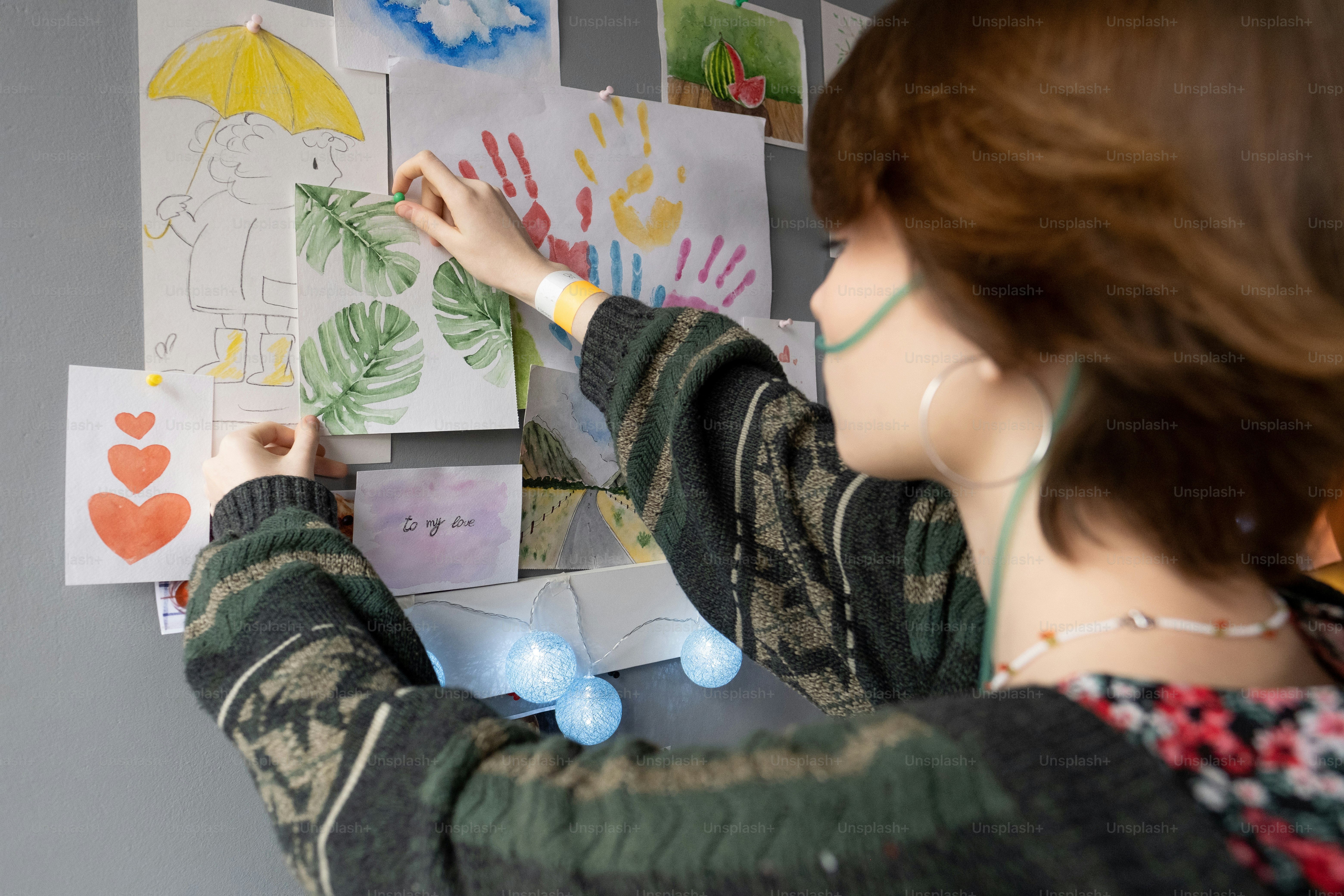Teenage female patient of hospital hanging drawing of green leaves on wall by her bed in ward of intensive therapy
