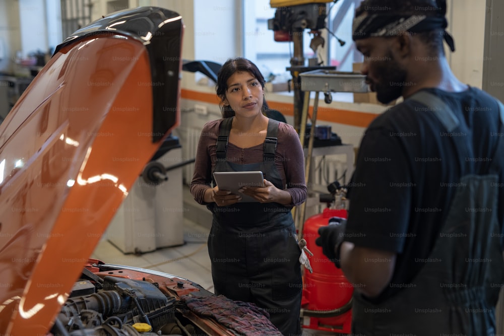 Retrato de cintura para arriba de una mecánica femenina usando una tableta digital mientras inspecciona el automóvil en el taller de reparación de automóviles