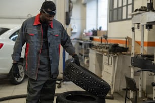 Portrait of tough black mechanic changing tires on car while working in auto repair shop, copy space