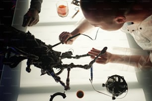 Hände einer jungen Cyberpunk-Frau mit elektrischem Instrument, die elektronische Geräte repariert, während sie sich darüber beugt
