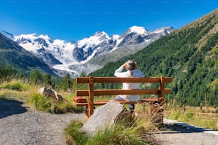 An elderly tourist observes the mountains with a telescope from a bench