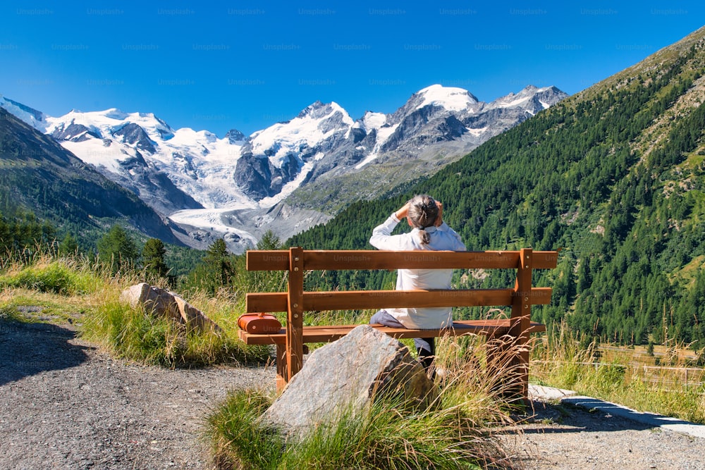 An elderly tourist observes the mountains with a telescope from a bench