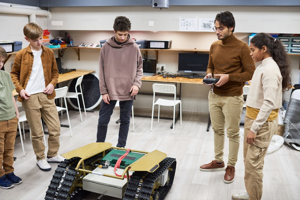 Retrato de corpo inteiro do grupo diversificado de adolescentes que operam o robô de controle remoto na aula de engenharia na escola