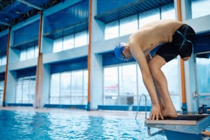 Swimmer with a leg disability on starting block preparing to jump into the pool. Copy space.