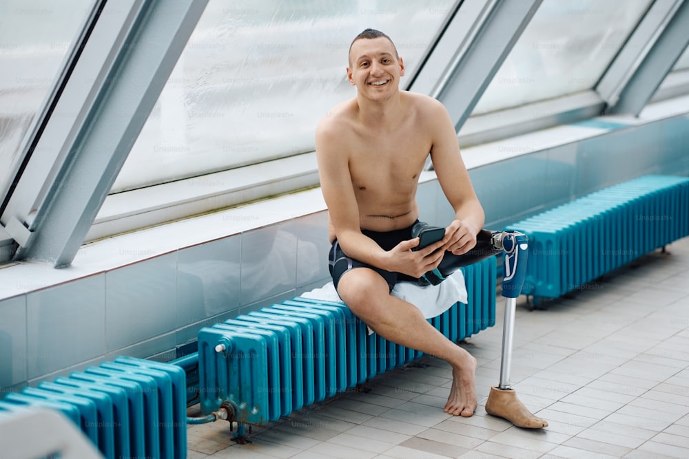 스포츠 훈련 후 휴대폰으로 인공 다리 문자를 보내고 카메라를 보고 있는 행복한 수영 선수.