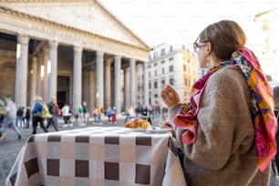 Woman having breakfast with croissant and coffee at outdoor cafe near famous Pantheon temple in Rome. Idea of spending time in Rome. Concept of italian lifestyle and travel