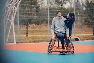 Uomo atletico felice con disabilità e la sua amica sul campo da basket all'aperto. Copia spazio.