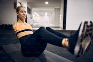Female athlete with disability exercising sit-ups while having sports training in a gym.